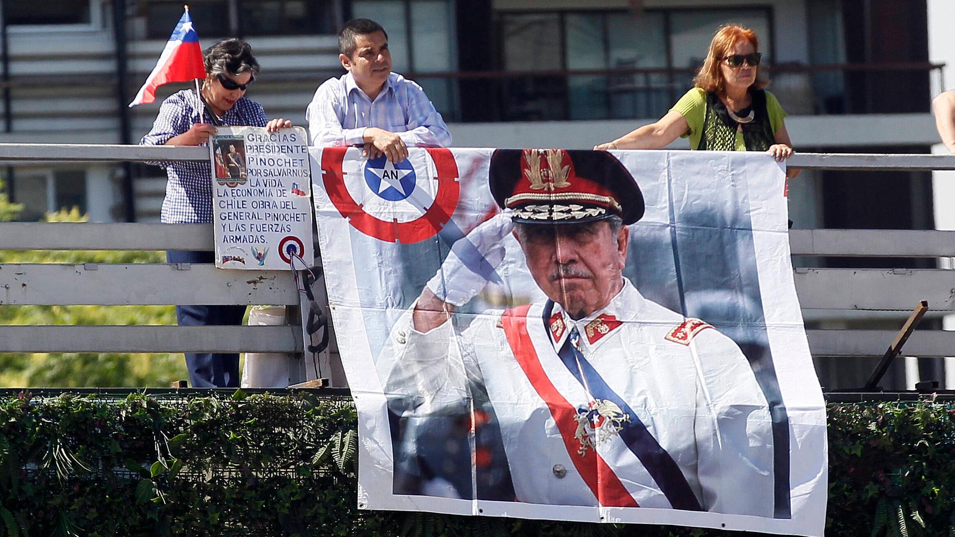 Zwei Personen hängen ein großes Plakat mit dem Bild von Augusto Pinochet ein Geländer hinrunter. Zwei Personen hängen ein großes Plakat mit dem Bild von Augusto Pinochet ein Geländer hinrunter.