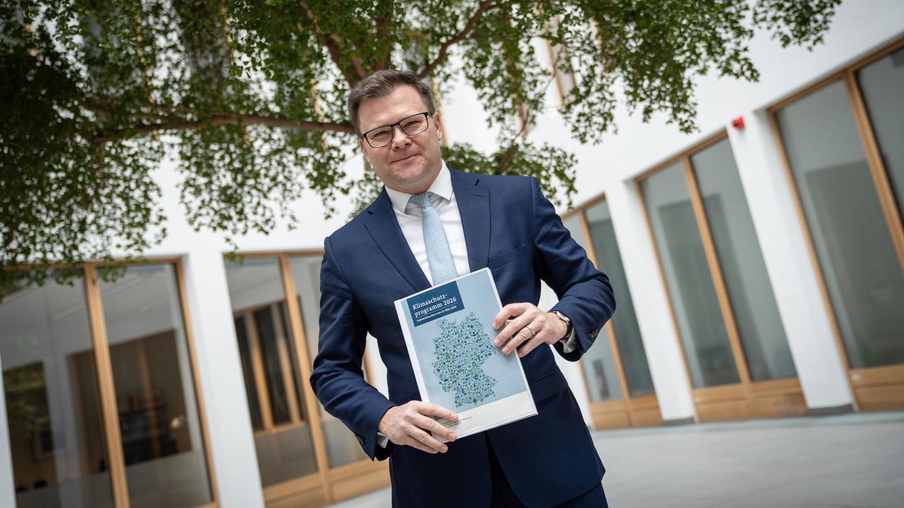 Umweltminister Carsten Schneider steht vor einem Baum und präsentiert eine Broschüre.