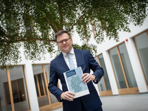 Umweltminister Carsten Schneider steht vor einem Baum und präsentiert eine Broschüre.