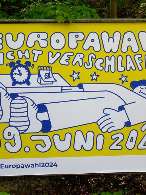 Auf einem Wahlplakat zur Europawahl 2024 ist eine gezeichnete Figur zu sehen, die schläft und vom Wecker pünktlich geweckt wird, um an der Wahl teilzunehmen.