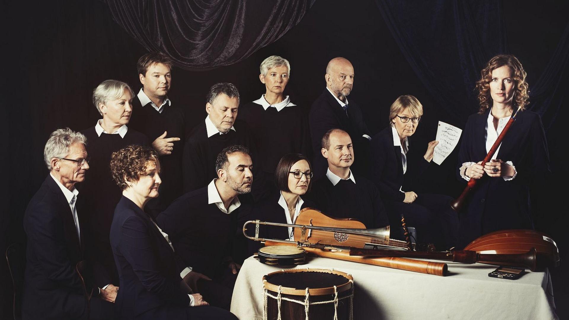Das Ensemble hat sich in dunklen Kleidern wie auf einem Rembrandgemälde in eine Gruppe um einen Tisch gesetzt, auf dem Musikinstrumente der Renaissance liegen.