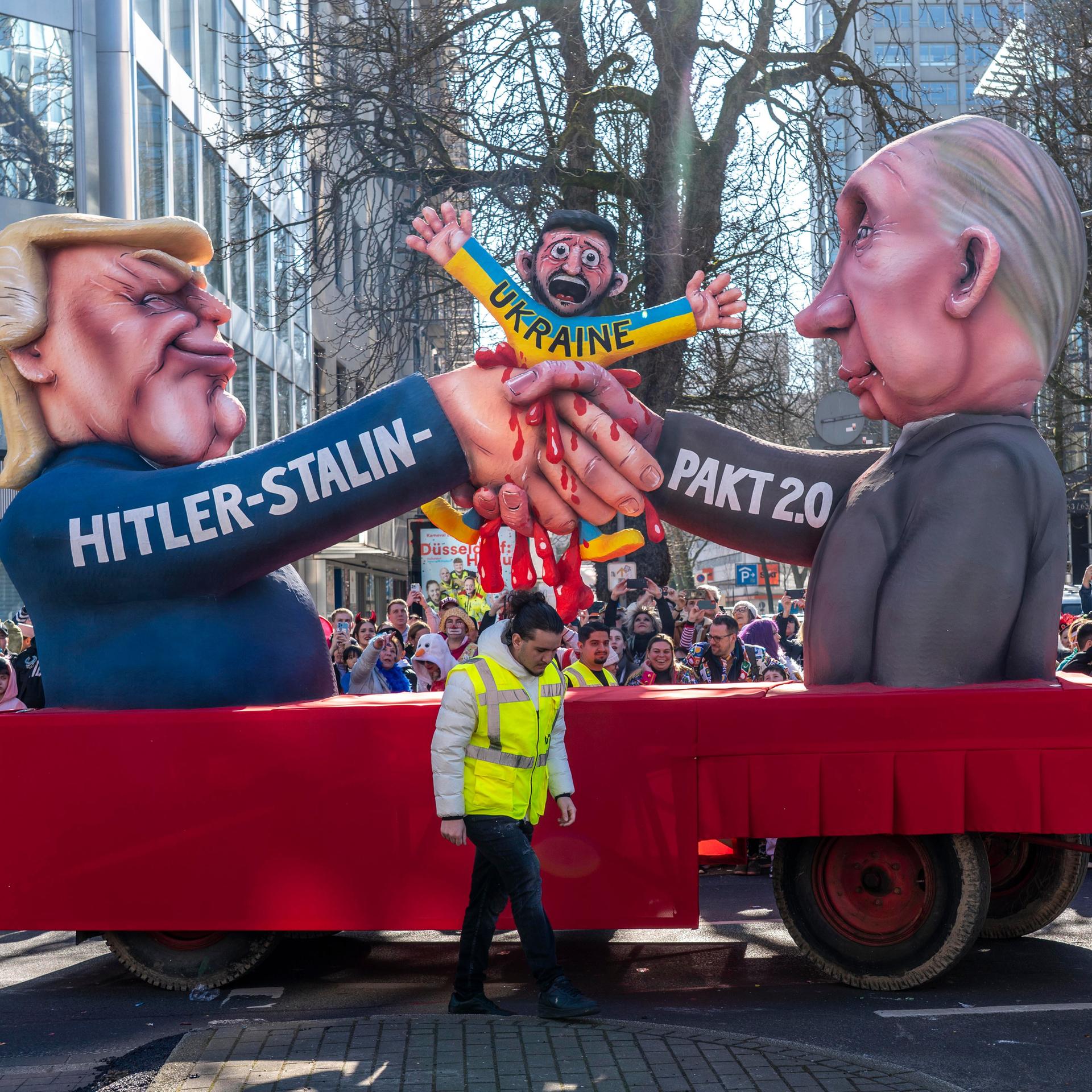 Der Mottowagen von Wagenbauer Jacques Tilly beim Rosenmontagszug in Düsseldorf: Putin und Trump geben sich die Hand und zerquetschen dabei den Präsidenten der Ukraine, Selenskyj. 