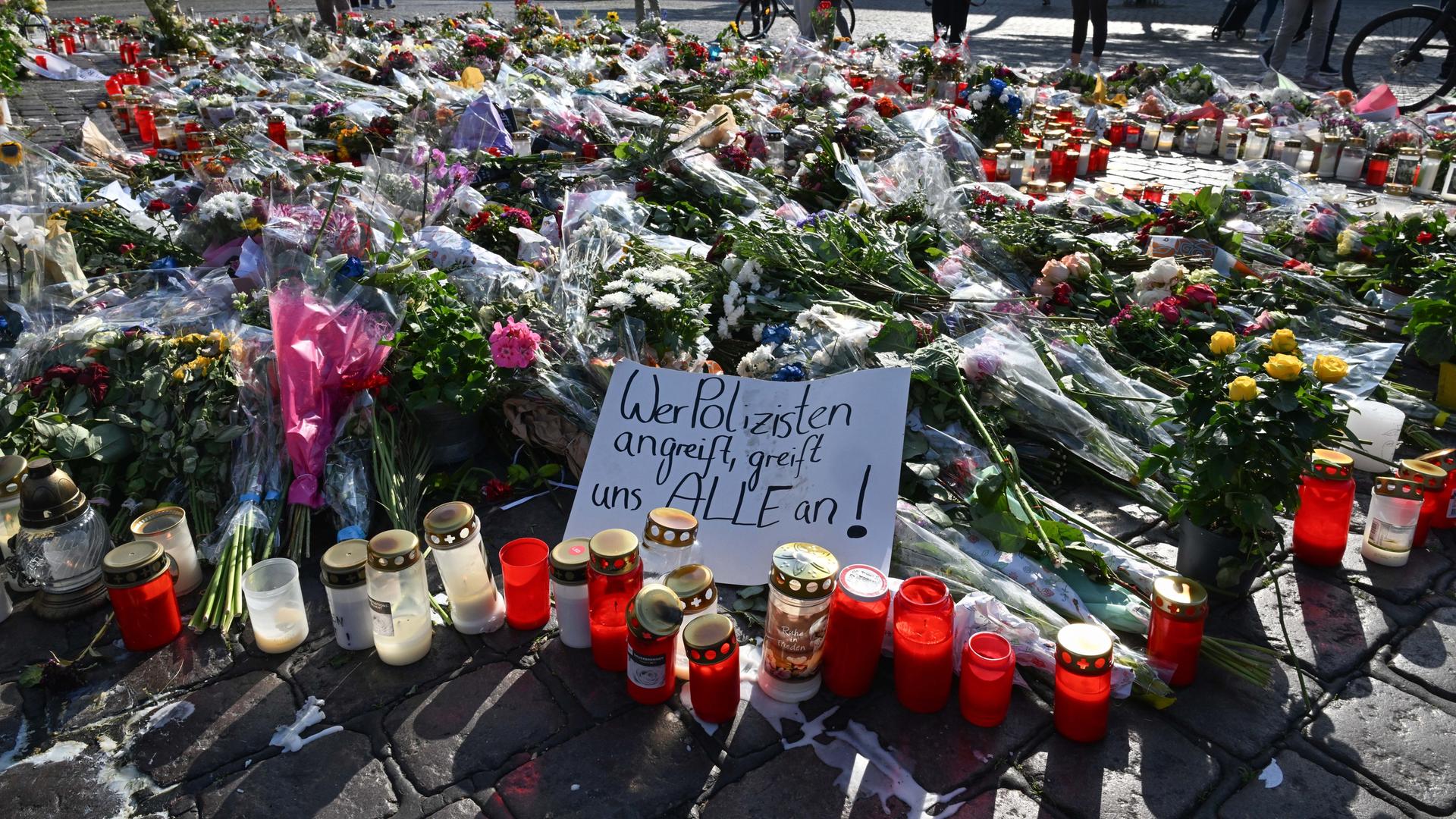 Blumen und Kerzen liegen auf dem Marktplatz. Auf einem Zettel steht geschrieben "Wer Polizisten angreift, greift uns alle an!"