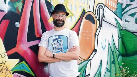 Der Musiker P.R. Kantate, bürgerlicher Name Richard Haus, steht im Görlitzer Park in Berlin-Kreuzberg vor einer bunten Graffitiwand.