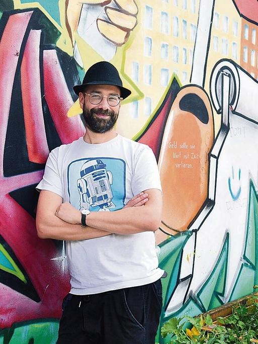 Der Musiker P.R. Kantate, bürgerlicher Name Richard Haus, steht im Görlitzer Park in Berlin-Kreuzberg vor einer bunten Graffitiwand. Der Musiker P.R. Kantate, bürgerlicher Name Richard Haus, steht im Görlitzer Park in Berlin-Kreuzberg vor einer bunten Graffitiwand.