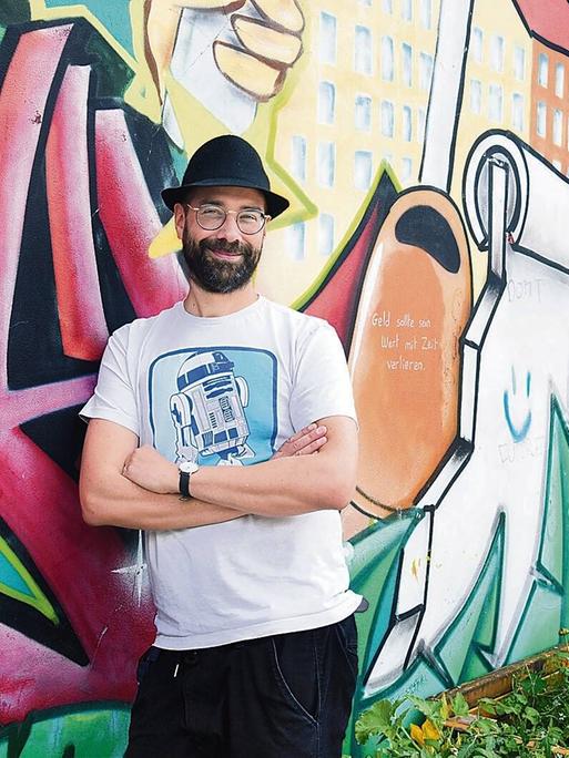 Der Musiker P.R. Kantate, bürgerlicher Name Richard Haus, steht im Görlitzer Park in Berlin-Kreuzberg vor einer bunten Graffitiwand.