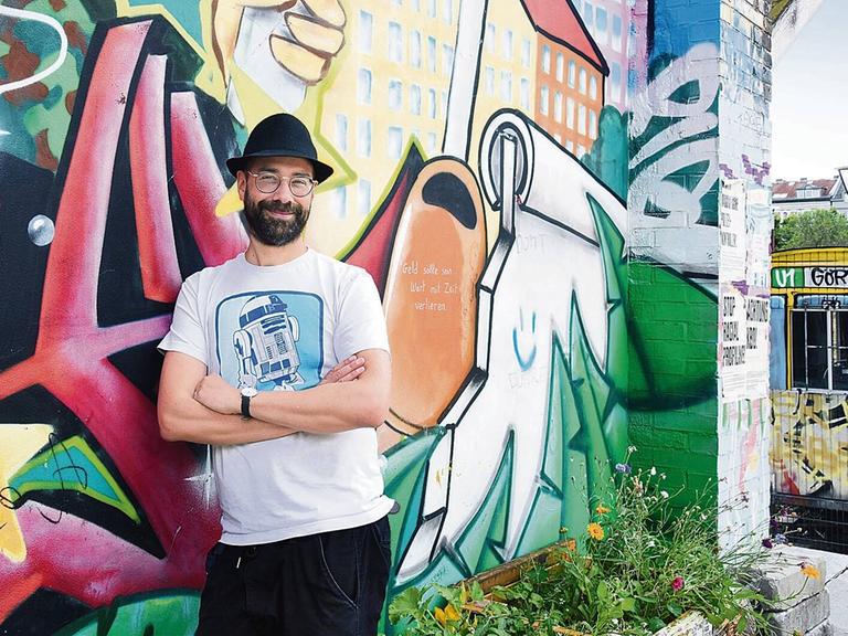 Der Musiker P.R. Kantate, bürgerlicher Name Richard Haus, steht im Görlitzer Park in Berlin-Kreuzberg vor einer bunten Graffitiwand.