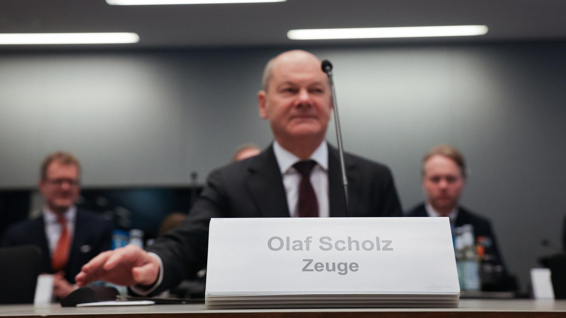 Ein Mann sitzt an einem Tisch. Vor ihm ist ein Schild. Darauf steht: "Olaf Scholz. Zeuge". Es ist Bundeskanzler Olaf Scholz (SPD) bei einer Sitzung des Parlamentarischen Untersuchungsausschusses "Cum-Ex".