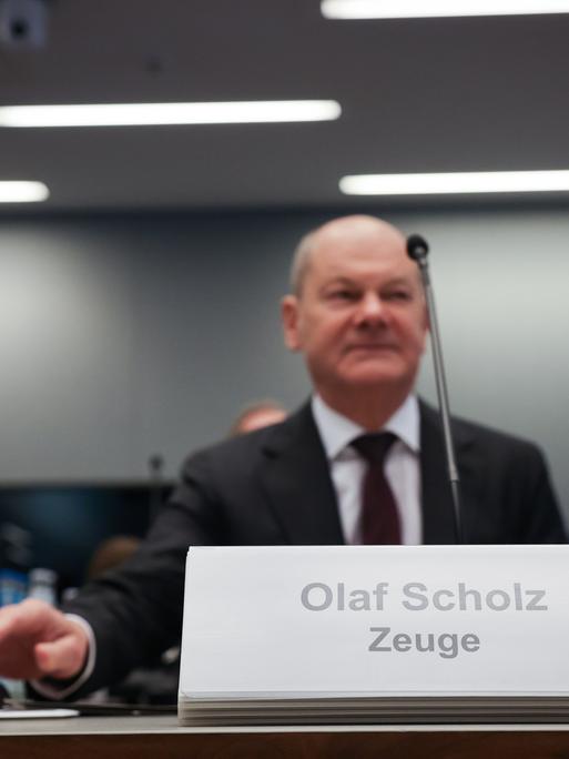 Ein Mann sitzt an einem Tisch. Vor ihm ist ein Schild. Darauf steht: "Olaf Scholz. Zeuge". Es ist Bundeskanzler Olaf Scholz (SPD) bei einer Sitzung des Parlamentarischen Untersuchungsausschusses "Cum-Ex".