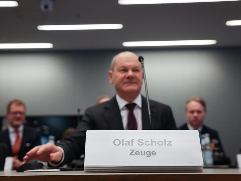 Ein Mann sitzt an einem Tisch. Vor ihm ist ein Schild. Darauf steht: "Olaf Scholz. Zeuge". Es ist Bundeskanzler Olaf Scholz (SPD) bei einer Sitzung des Parlamentarischen Untersuchungsausschusses "Cum-Ex".