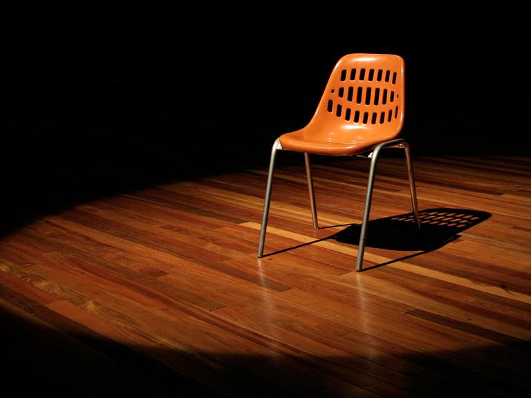 Ein leerer Stuhl steht auf einer Theaterbühne.