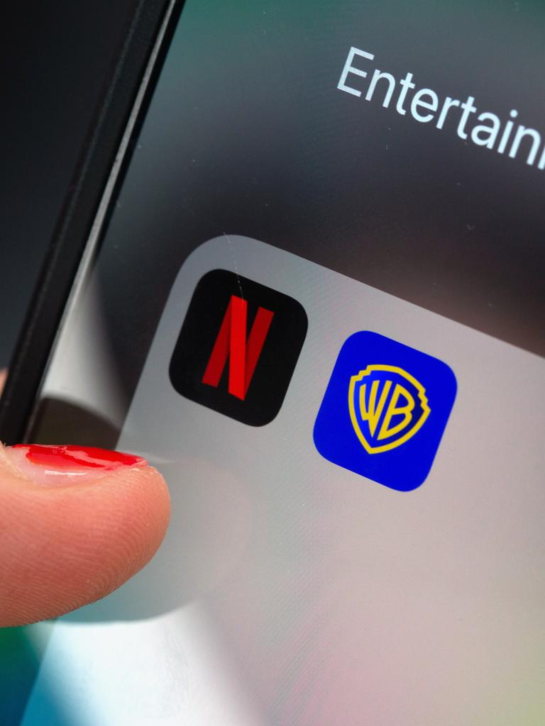 Ein Finger tippt auf einem Smartphone auf ein App-Ordnerfeld mit den Logos der Streamingplattform Netflix (links) und des Filmstudios Warner Brothers (rechts). 
