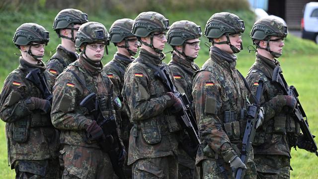 8 junge Soldaten stehen dicht nebeneinander. Sie tragen Uniform und sind bewaffnet.