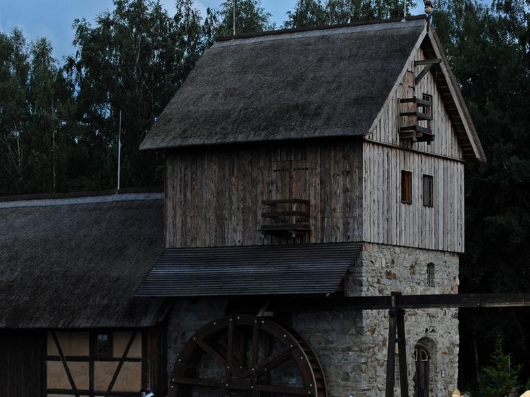 Aufnahme der Schwarzen Mühle in der Lausitz bei Dämmerlicht. Das Mühlhaus ist aus Stein und Holz gebaut, an der Seite hängt ein Mühlrad.