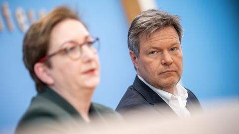 Man sieht die beiden Köpfe nebeneinander: Links unscharf Geywitz, rechts scharf Habeck. Geywitz sagt etwas, Habeck hört zu. Dahinter die blaue Wand der Bundespressekonferenz.