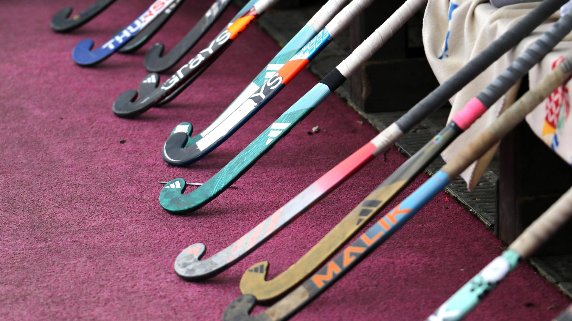 Hockeyschläger lehnen an einer Bank, während das Team beim Warmmachen ist.