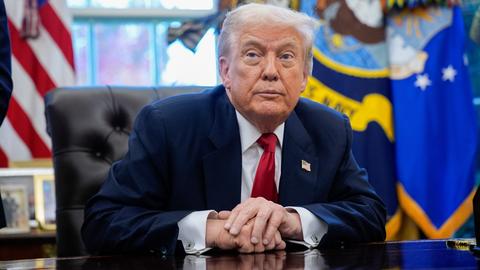 US-Präsident Trump sitzt an seinem Schreibtisch und blickt schräg an der Kamera vorbei.