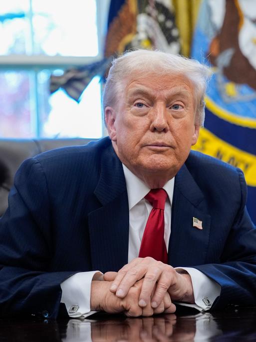 US-Präsident Trump sitzt an seinem Schreibtisch und blickt schräg an der Kamera vorbei.