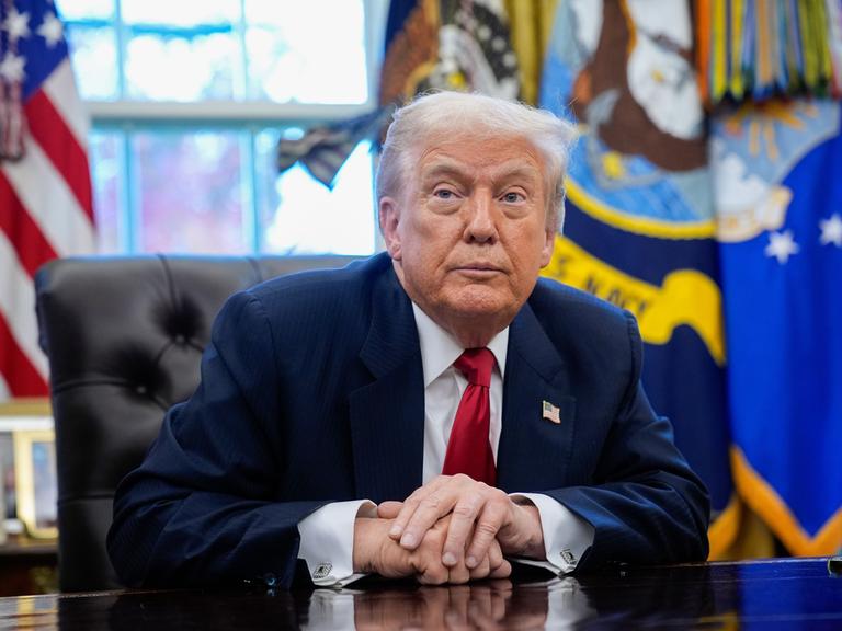 US-Präsident Trump sitzt an seinem Schreibtisch und blickt schräg an der Kamera vorbei.