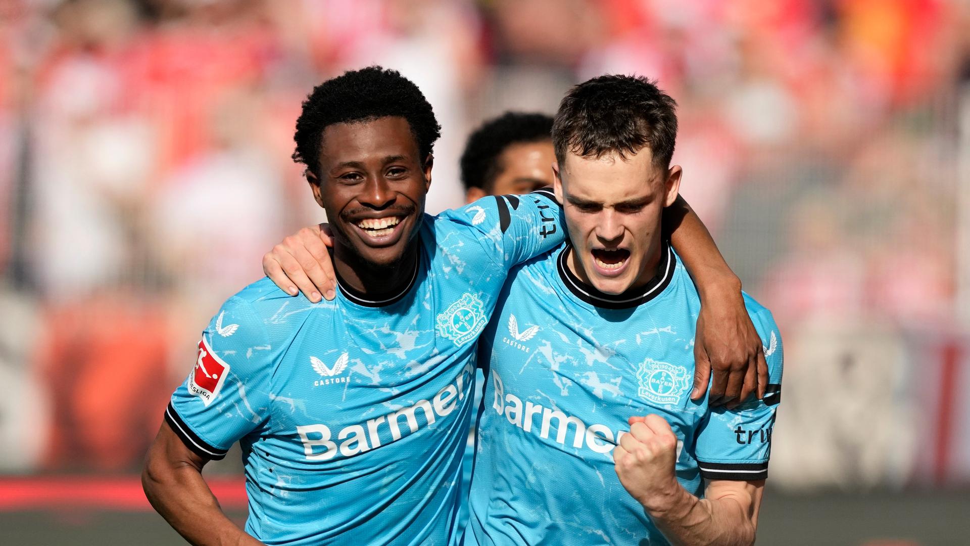 Nathan Tella (li.) und Florian Wirtz (re.) haben die Arme umeinander gelegt und freuen sich. Nathan Tella (li.) und Florian Wirtz (re.) haben die Arme umeinander gelegt und freuen sich.