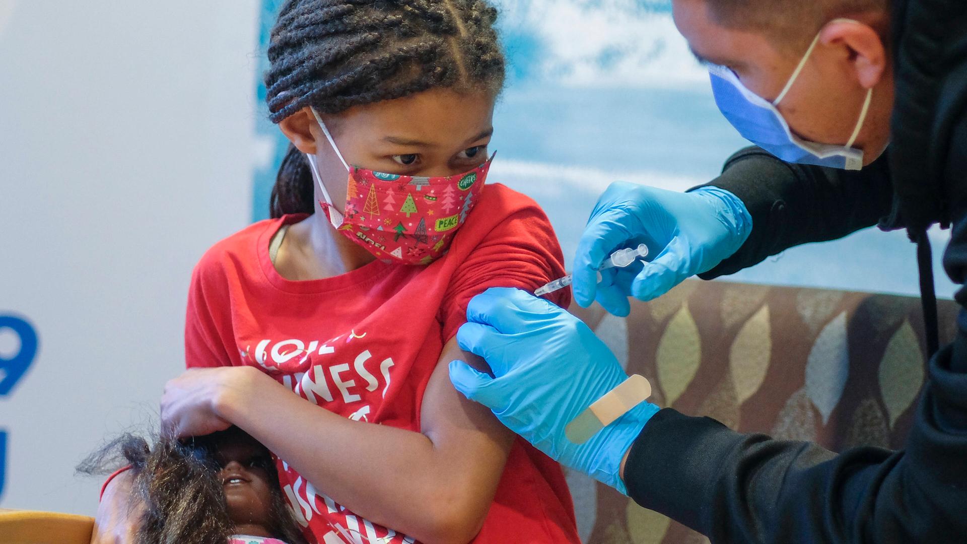 Ein Mädchen hält ihre Puppe während sie eine Impfung bekommt.