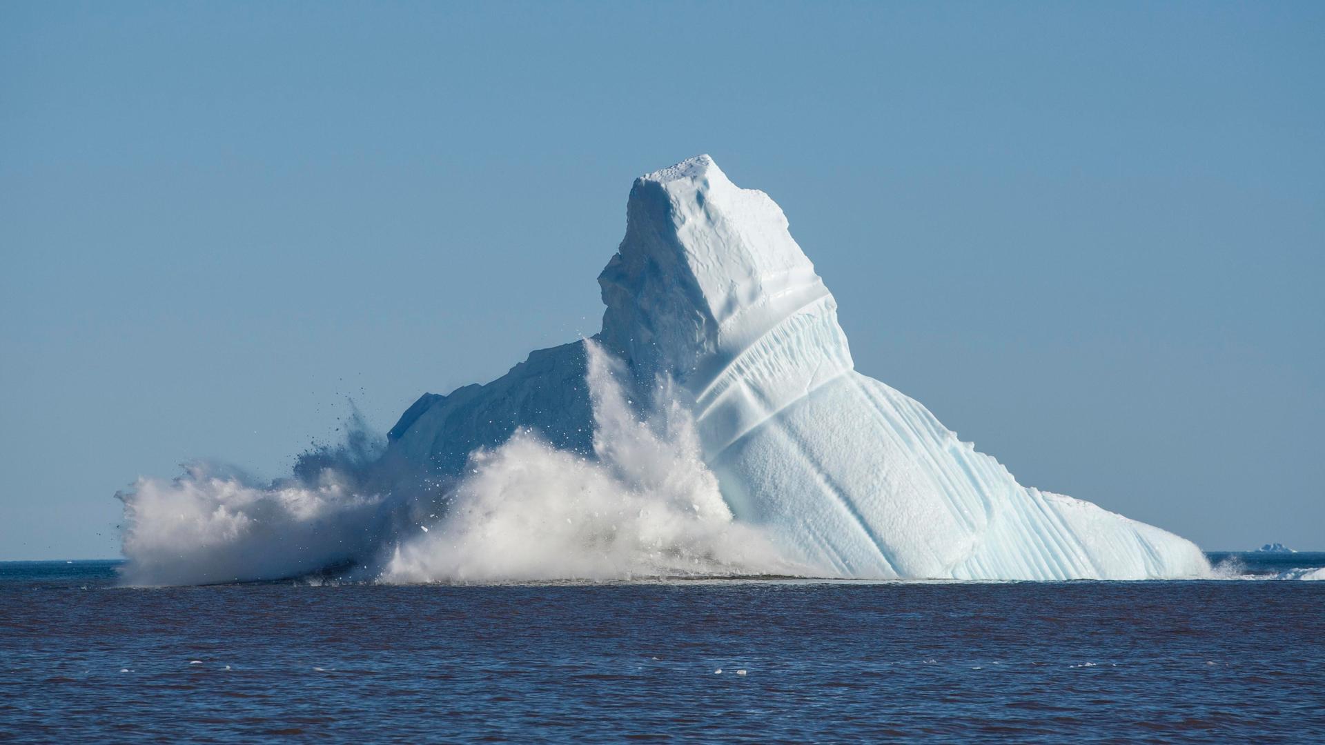 Eismassen vor einer Bucht in Grönland brechen von einem enormen Eisberg ab