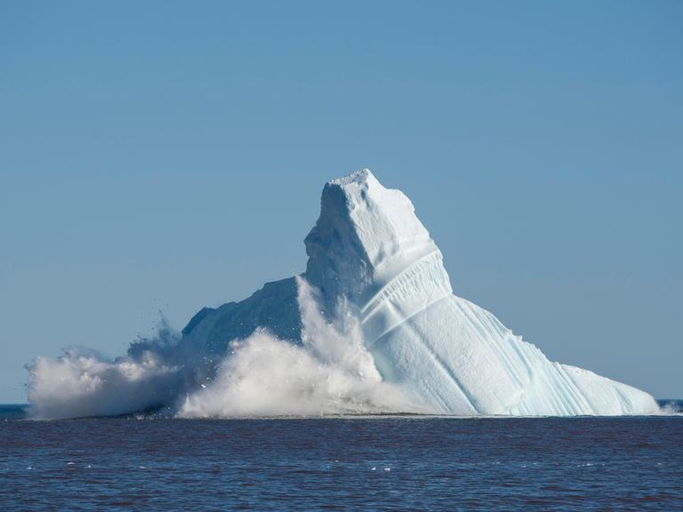 Eismassen vor einer Bucht in Grönland brechen von einem enormen Eisberg ab