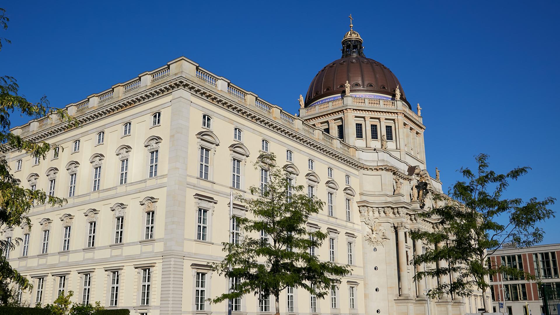 Blick auf das Humboldt Forum in Berlin-Mitte, das eine Rekonstruktion des alten Berliner Stadtschlosses ist. Im Vordergrund sind einige Bäume zu sehen. 