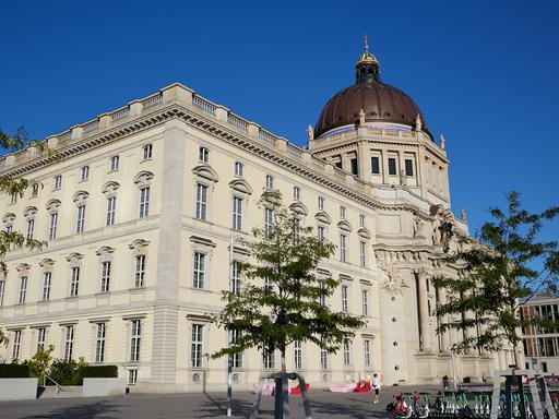 Blick auf das Humboldt Forum in Berlin-Mitte, das eine Rekonstruktion des alten Berliner Stadtschlosses ist. Im Vordergrund sind einige Bäume zu sehen. 