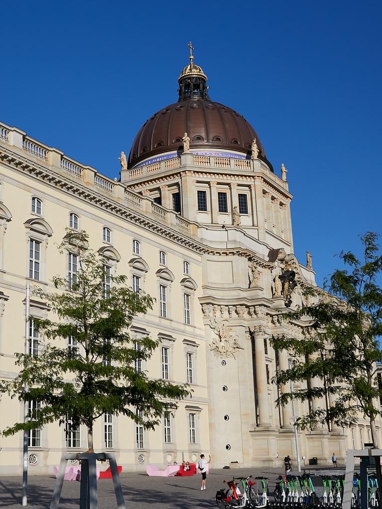 Blick auf das Humboldt Forum in Berlin-Mitte, das eine Rekonstruktion des alten Berliner Stadtschlosses ist. Im Vordergrund sind einige Bäume zu sehen. 