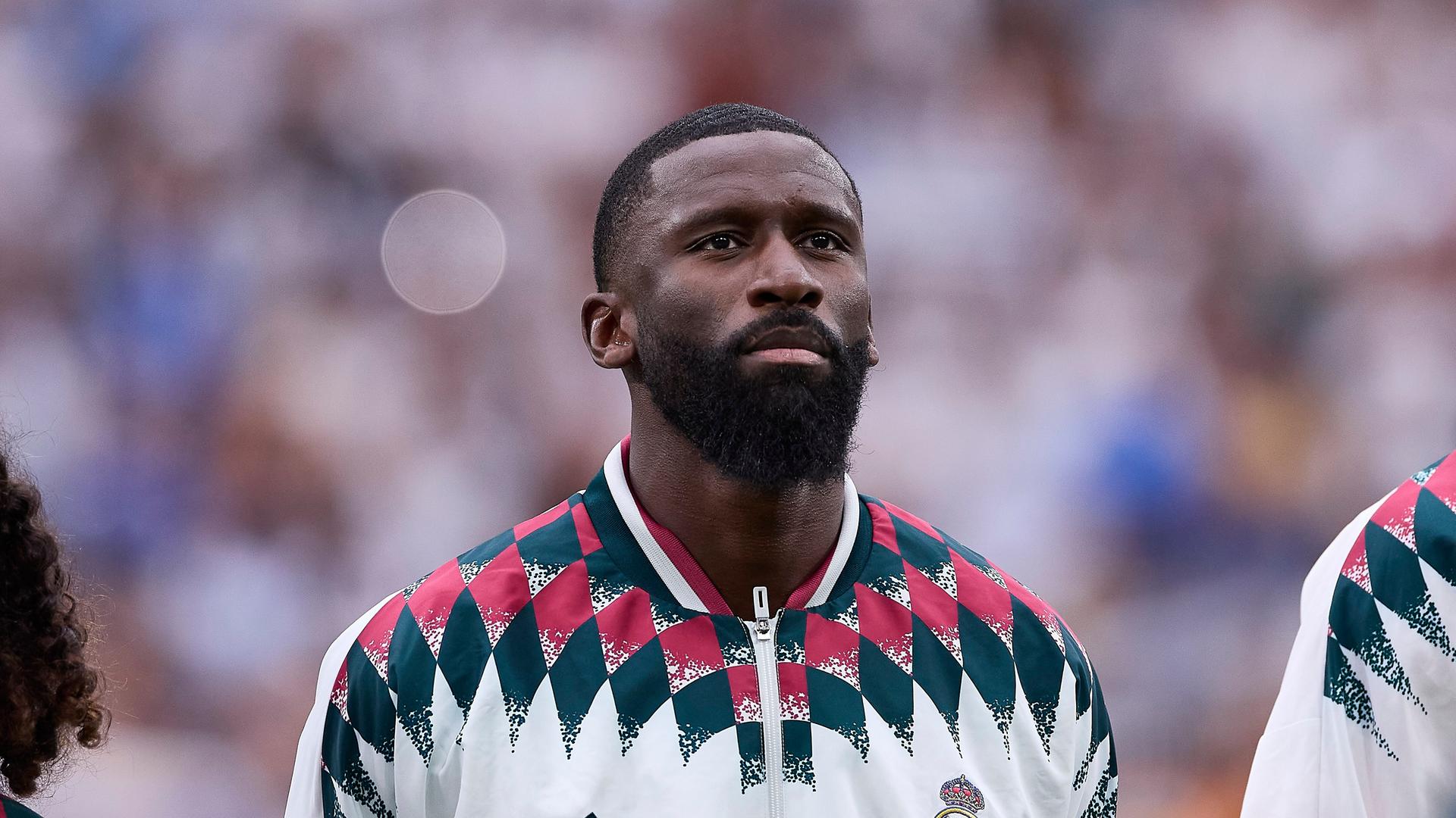 Antonio Rüdiger steht zwischen zwei anderen Fußballspielern, er trägt eine weiße Trikotjacke. Antonio Rüdiger steht zwischen zwei anderen Fußballspielern, er trägt eine weiße Trikotjacke.