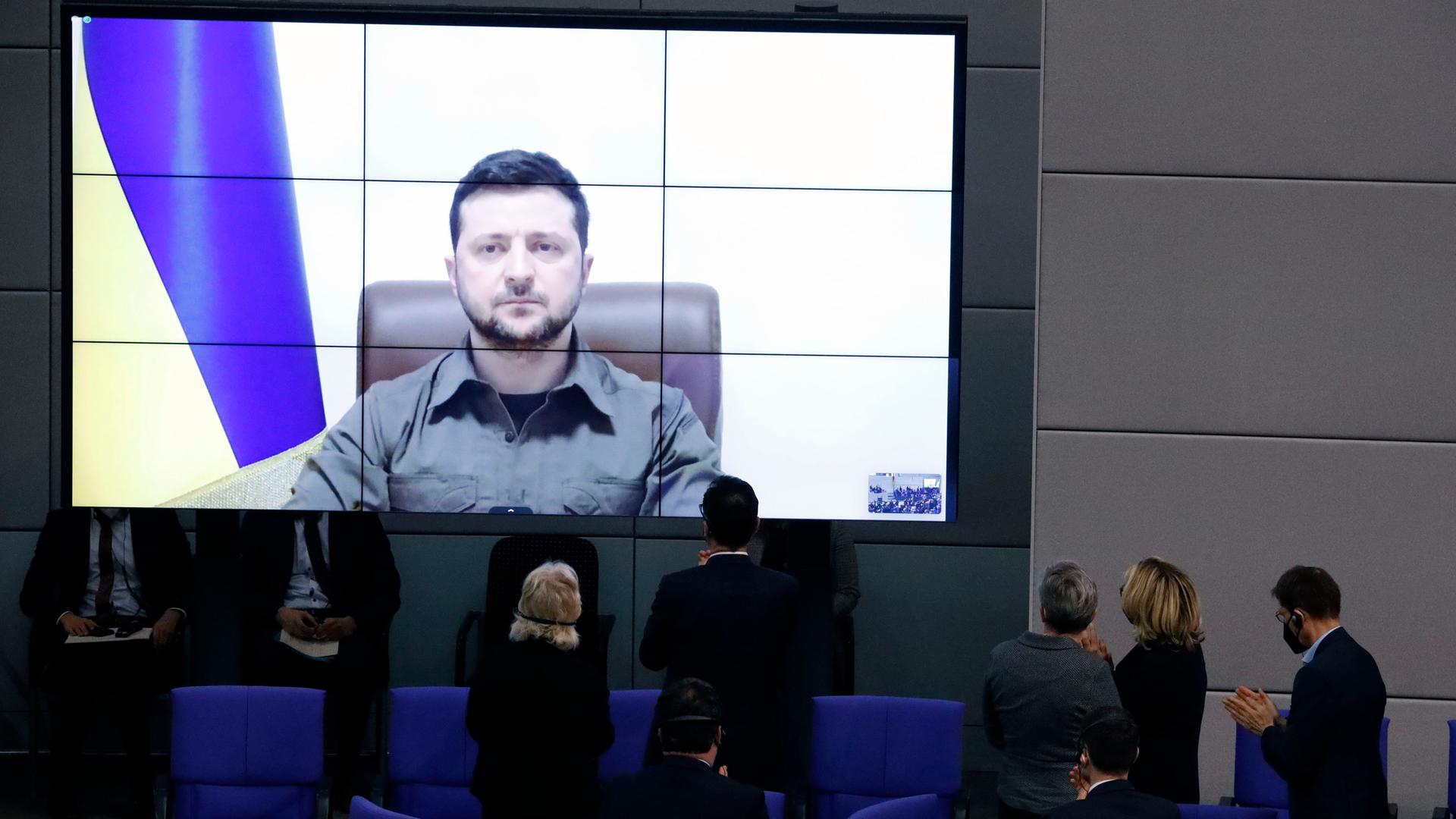 Der Präsident der Ukraine, Selenskyj, auf einem großen Bildschirm, davor stehend Abgeordnete des Bundestages
