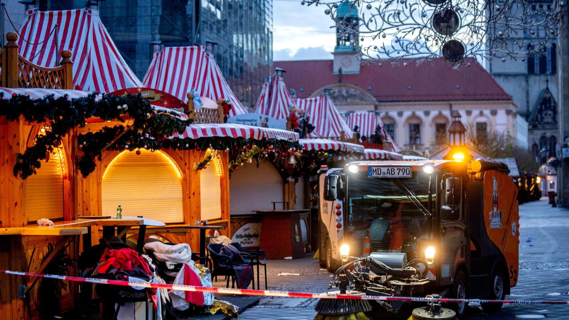 Das Bild zeigt eine Budengasse auf dem Weihnachtsmarkt in Magdeburg, in der gerade städtische Reinigungsarbeiten stattfinden.