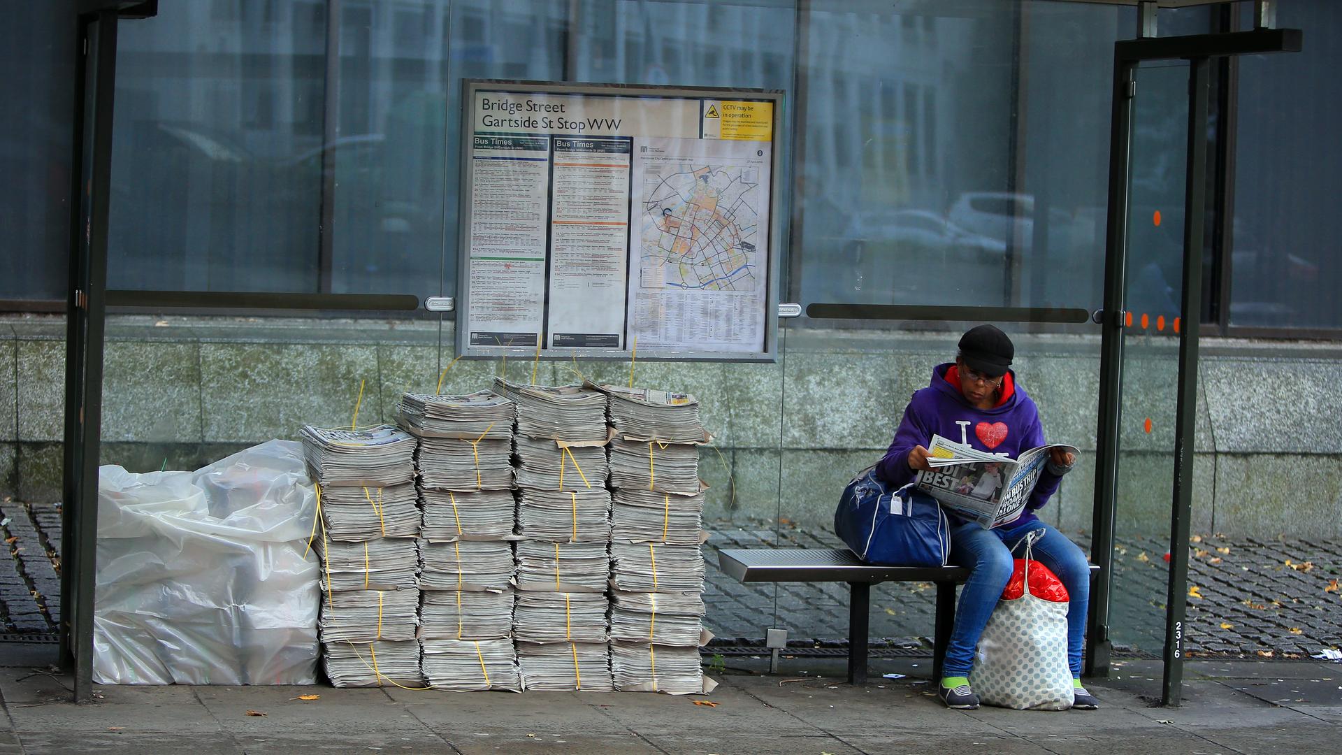 Eine Frau blättert in einer Zeitung, während sie in Manchester auf den Bus wartet.