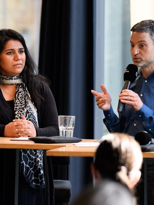 Saba-Nur Cheema und Meron Mendel sitzen bei einer Pressekonferenz nebeneinander an einem Podium.