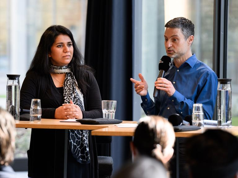 Saba-Nur Cheema und Meron Mendel sitzen bei einer Pressekonferenz nebeneinander an einem Podium.