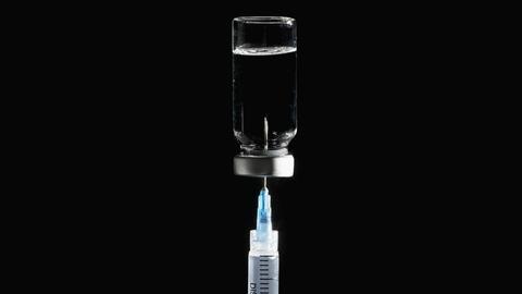 Spritze in Covid-19-Impfstoffflasche auf schwarzem Hintergrund.