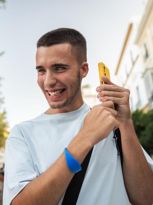 Ein junger Mann nimmt fröhlich eine Sprachnachricht auf seinem Smartphone auf, während er durch einen Stadtpark spaziert. Ein junger Mann nimmt fröhlich eine Sprachnachricht auf seinem Smartphone auf, während er durch einen Stadtpark spaziert.