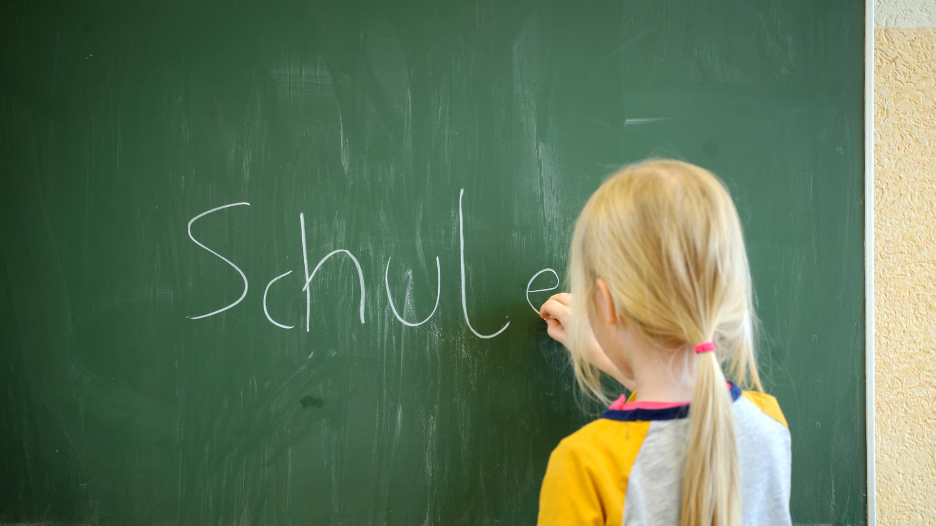 Ein Mädchen schreibt mit Kreide an eine Schultafel das Wort "Schule" Ein Mädchen schreibt mit Kreide an eine Schultafel das Wort "Schule"