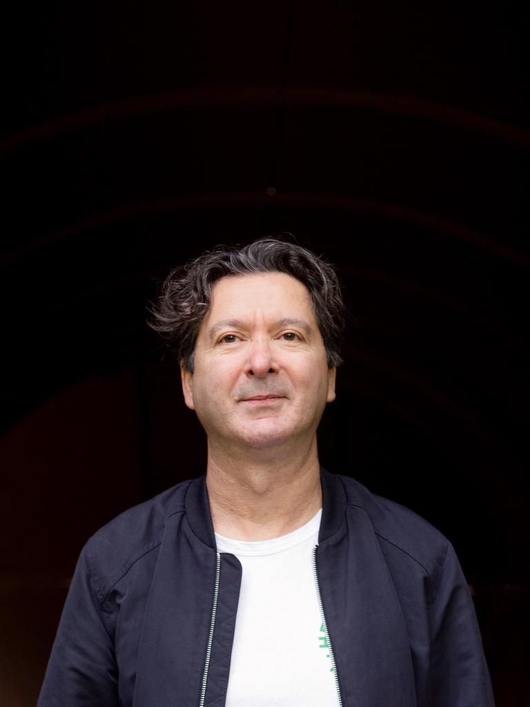 Mustafa Akça vor schwarzem Hintergrund in blauer Jacke.