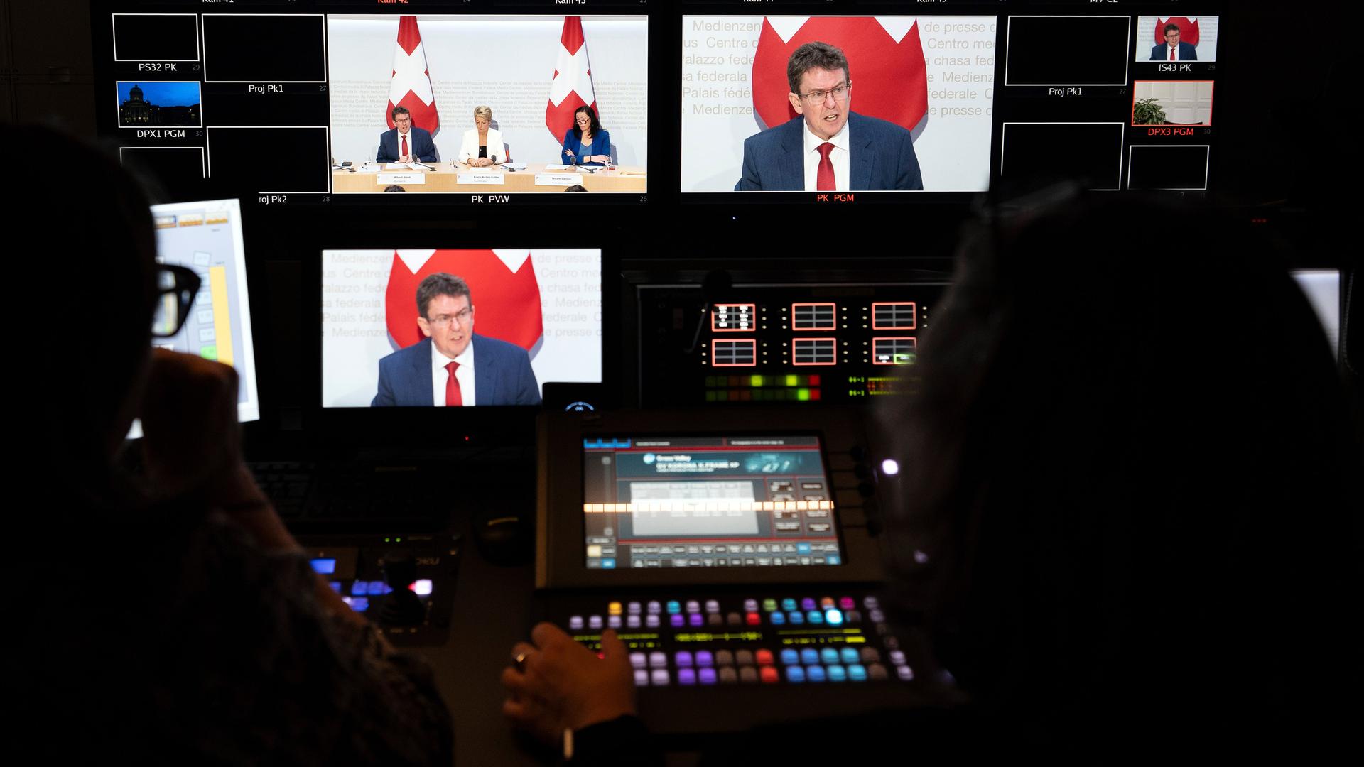 In der Bildregie des Fernsehens sind das Bildmischpult und zahlreiche Bildschirme zu sehen: Auf den Bildschirmen: Bundesrat Albert Rösti vor einer Schweizer Flagge