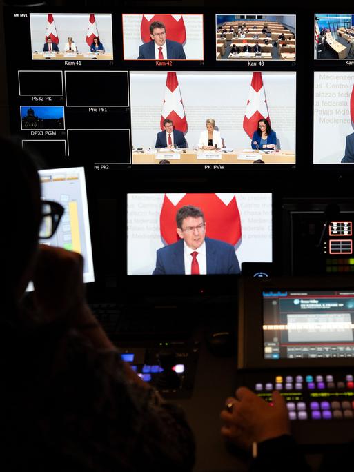 In der Bildregie des Fernsehens sind das Bildmischpult und zahlreiche Bildschirme zu sehen: Auf den Bildschirmen: Bundesrat Albert Rösti vor einer Schweizer Flagge