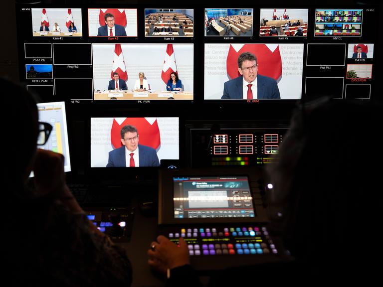 In der Bildregie des Fernsehens sind das Bildmischpult und zahlreiche Bildschirme zu sehen: Auf den Bildschirmen: Bundesrat Albert Rösti vor einer Schweizer Flagge