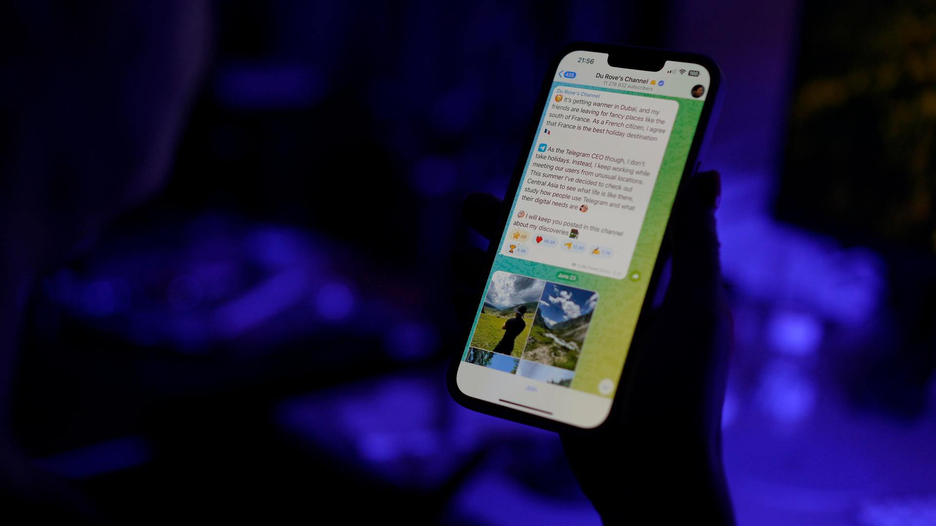 Der Telegram-Messengerdienst ist auf dem Display eines Smartphones zu sehen, dass eine Person in der Hand hält. Die Person ist nur als Schattenumriss zu erkennen, der Hintergrund schimmert bläulich.