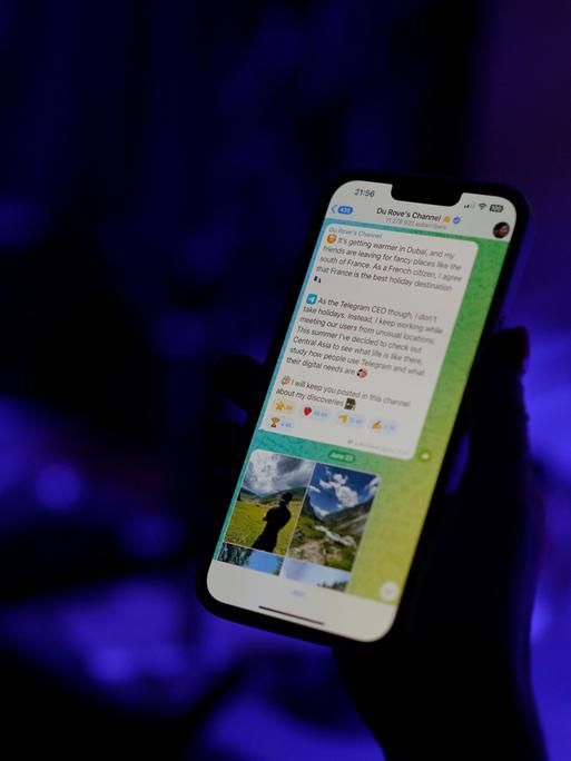 Der Telegram-Messengerdienst ist auf dem Display eines Smartphones zu sehen, dass eine Person in der Hand hält. Die Person ist nur als Schattenumriss zu erkennen, der Hintergrund schimmert bläulich.