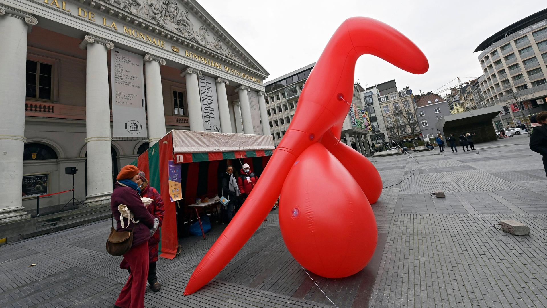 Das Bild zeigt ein übergroßes, rotes aufblasbares Modell einer weiblichen Klitoris, das auf einem Platz in Brüssel steht. 