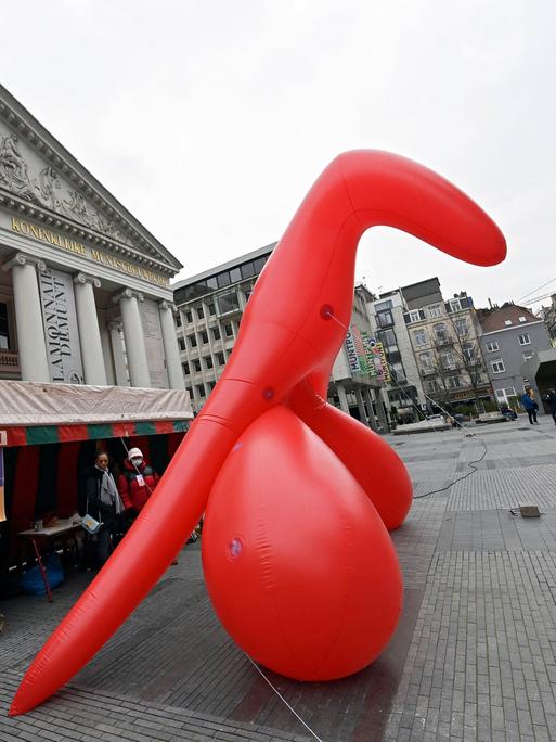 Das Bild zeigt ein übergroßes, rotes aufblasbares Modell einer weiblichen Klitoris, das auf einem Platz in Brüssel steht. 