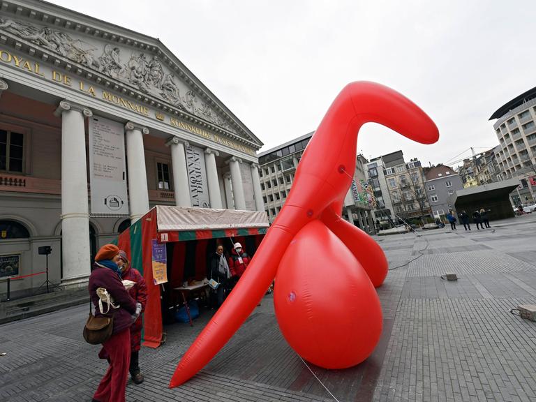 Das Bild zeigt ein übergroßes, rotes aufblasbares Modell einer weiblichen Klitoris, das auf einem Platz in Brüssel steht. 