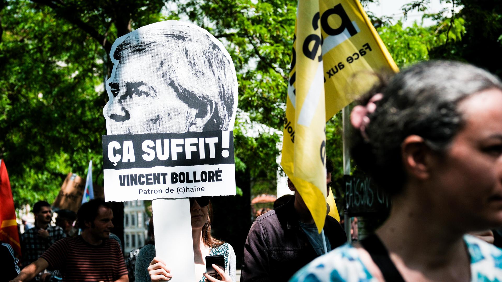 Eine Demonstrantin hält ein Transparent mit der Aufschrift "Vincent Bolloré – Es reicht" ("Chef des Hasses") in die Höhe.

