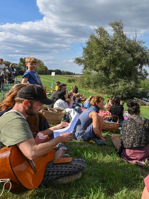 Menschen sitzen auf dem Oder-Deich, im Vordergrund ein Mann mit Gitarre, an einer anderen Stelle steht eine Trommel.